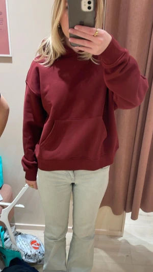 Vinröd hoodie med huva och ficka - Säljer en vinröd hoodie med stor magficka och huva. Tröjan har en loose passform och är tillverkad i mjuk bomull, perfekt för chill dagar. Långärmad modell med ribbade muddar vid ärmslut och nederkant.