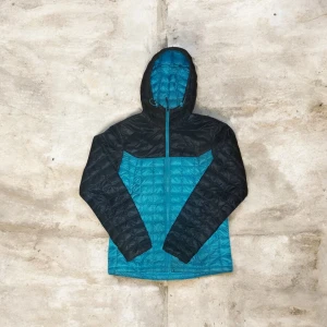 Blå och svart dunjacka från The North Face - Säljer en blå och svart dunjacka från The North Face med huva och dragkedja. Jackan är quiltad och har en sportig look med kontrastfärgade partier. Perfekt för kyliga dagar och outdoor-äventyr. Klassisk passform och lätt att bära med sig.