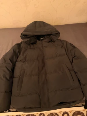 Mörkrgrå pufferjacka från Canada Goose Macmillan black badge - Säljer en mörkgrå pufferjacka från Canada Goose med luva och snyggt broderat märke på ärmen. Jackan har dragkedja, två sidofickor och quiltad design, perfekt för kalla dagar. Jag beställde denna jacka och den passa inte mig det är anledningen till varför jag säljer denna jacka den är extremt varm storleken är M fick hem den den 26 november så den är helt ny och passar inte någon familjemedlem därför säljer jag den. Pris går att diskuteras.
