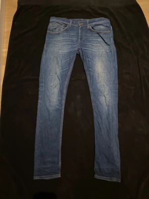 Dondup Blå - Säljer ett par blå skinny jeans med snygga slitningar och klassisk femficksdesign. Jeansen har smal passform och är tillverkade i mjukt denimtyg med lite stretch för extra komfort. Perfekt för dig som gillar en modern och tajt look.