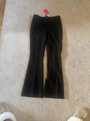 Svarta bootcut kostymbyxor S - Snygga svarta kostymbyxor i bootcut-modell med klassisk passform och pressveck. Byxorna har bälteshällor, dold dragkedja och knapp framtill samt ficka bak. Perfekta för en clean och stilren look.