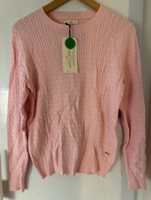Ny kabelstickad tröja från Lindex, Holly & White st. S - Säljer en ny ljusrosa kabelstickad tröja från Lindex,  Holly & White. Tröjan har rund halsringning, långa ärmar och ribbade muddar. Perfekt för dig som gillar klassisk och söt stil. Materialet är mjukt och skönt i bomull.  80% bomull, 20% polyamid
