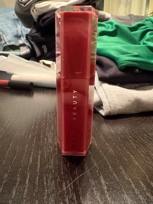 Fenty Beauty Gloss Bomb Stix Riri - Fenty Beauty Gloss Bomb Stix i färgen Riri (06), en high-shine gloss stick med ultra-glansig finish. Kommer i en snygg, sexkantig hylsa i transparent röd plast. Perfekt för att ge läpparna en glansig, mjuk look med hint av rosa-nude.