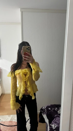 Gul offshoulder volangblus med knyt - Säljer en superfin gul blus med offshoulder och långa ärmar. Toppen har volanger längs halsringningen och ärmsluten, samt en snygg knytning framtill. Materialet är lätt och krusat, vilket ger en cool och luftig känsla. Perfekt för dig som gillar färg och statement-plagg!