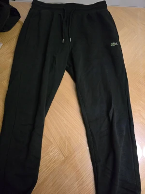 Lacoste - Svarta mjukisbyxor från Lacoste med klassisk krokodillogga på benet. Perfekta för chill eller träning, med en clean och stilren look.