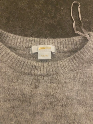 Grå stickad tröja Gina Tricot - En enkel och snygg grå stickad tröja från Gina Tricot i storlek 146/152. Tröjan har korta ärmar, rund hals och ribbade kanter. Perfekt för dig som gillar en clean och chill stil. Materialet är mjukt och känns skönt mot huden.