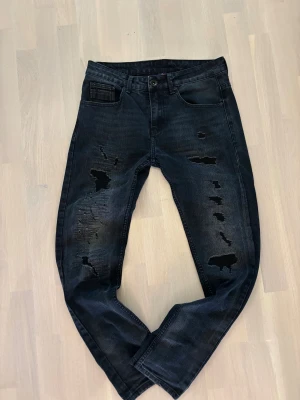 Vintage jeans - Snygga svarta jeans med slitningar och hål på både fram- och baksida av benen. Modellen har klassisk femficksdesign och raka ben. Jeansen har en cool, mörk tvätt och är perfekta för dig som gillar en edgy streetstil.