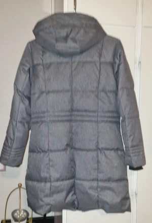 Grå pufferjacka från Tribute - Säljer en grå pufferjacka från Tribute med huva och dragkedja. Jackan har quiltad design, långa ärmar och praktiska fickor med dragkedja. Perfekt för kalla dagar och har en snygg, modern look.