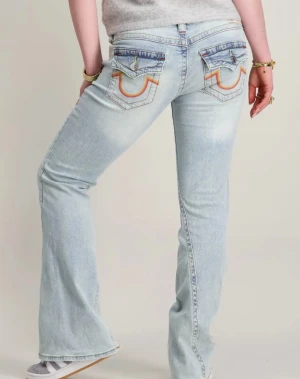 True religion jeans med röda fickor  - Snygga ljusblå bootcut jeans med broderade detaljer i röd, orange och gul på bakfickorna. Jeansen har klassisk femficksdesign och är tillverkade i mjukt denimtyg. Perfekt för dig som gillar retrovibbar och vill sticka ut med coola detaljer. Säljer pga att de är för låga för min smak. Pris kan diskuteras och kan skicka fler bilder💗