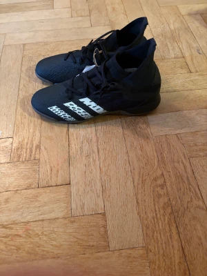 Adidas Predator Freak .3 IN fotbollsskor - Säljer ett par svarta Adidas Predator Freak .3 IN fotbollsskor i storlek 40. Skorna har vita detaljer med de klassiska tre ränderna på sidan och snörning. Ovandelen är i syntetmaterial och sulan är mönstrad för bra grepp på inomhusplan.