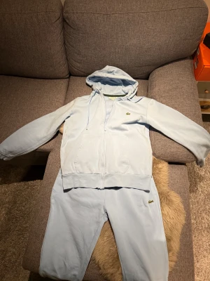 Ljusblå mjukisdress från Lacoste - Snygga ljusblå mjukisbyxor från Lacoste med slim fit-passning. Byxorna har resår i midjan och klassisk Lacoste-logga broderad på benet. Mjukt bomullsmaterial som är skönt att ha på sig, perfekt för chill eller träning.