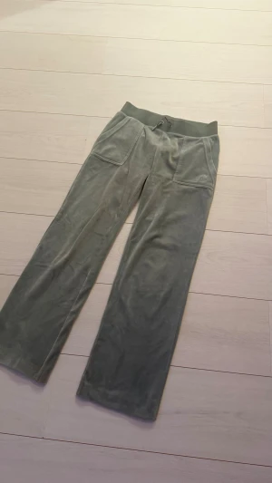 Gröna velourbyxor Juicy Couture XS - Snygga gröna mjukisbyxor från Juicy Couture i velour med bred resår och snörning i midjan. Byxorna har stora fickor fram och bak med dekorativa knappar. Perfekt för chill dagar och har en loose passform. Tyvärr en fläck på byxan. Nypris 1200. 