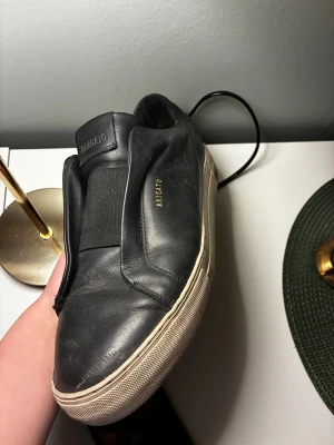 Svarta sneakers från Arigato i skinn - Svarta sneakers från Arigato med stilren design och vit platt sula. Skorna är tillverkade i mjukt skinn och har elastisk panel över vristen för enkel påtagning. Rund tå och diskret Arigato-logga i guld på sidan och under sulan.