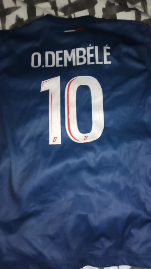 (Äkta 25/26) PSG Dembele #10 matchtröja Nike S - Paris Saint-Germain fotbollströja med O. Dembélé och nummer 10 på ryggen. Djupblå färg med röd och vit grafisk rand framtill, PSG-logga och Qatar Airways sponsortryck. Tillverkad i lätt polyester, kortärmad och med rund hals.