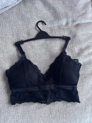 Svart spetsig linnetopp med justerbara band - Supersnygg svart linnetopp med spetsdetaljer och mesh. Toppen har v-ringad form och justerbara axelband för perfekt passform. Spetsen går runt hela nederkanten och ger en extra feminin touch. Perfekt att styla med jeans eller kjol för en cool look.70C