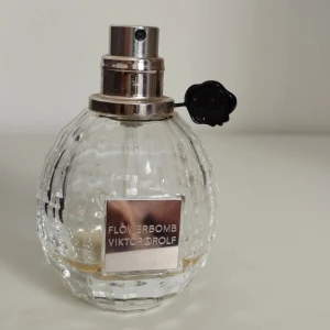 Nästan tom Flowerbomb parfym från Viktor & Rolf - Kul för den som vill testa eller vill ha en fin flaska på sminkbordet. Flowerbomb från Viktor & Rolf i en lyxig, facetterad glasflaska med metallisk spray och svart detalj. Flaskan rymmer 50 ml och har en elegant, transparent design med en silvrig etikett framtill. Doften är ikonisk och feminin.