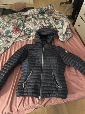 Mörkblå Colmar dunjacka med huva - Snygg mörkblå dunjacka från Colmar Originals med huva och två dragkedjeförsedda fickor. Jackan har quiltad design och logotyp på ärmen. Perfekt för kyliga dagar och har en stilren look som funkar till det mesta. även helt ny och aldrig använd. storlek 44 motsvarar xs/s priset går att diskutera vid snabbt köp