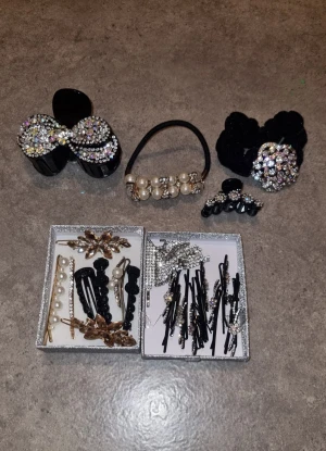 Glittriga håraccessoarer med pärlor - Säljer ett stort set med håraccessoarer, inklusive hårklämmor, hårsnoddar och hårspännen dekorerade med glittrande stenar, pärlor och blommor. Färgerna är mestadels svart, guld och silver med inslag av vita pärlor. Perfekt för att ge din frisyr extra bling och stil.