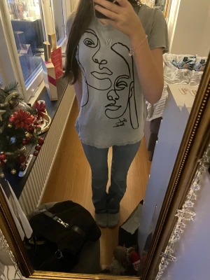 Grå t-shirt med tryck🩶 - Säljer en grå t-shirt med ett stort, svart konstnärligt ansiktstryck på framsidan. T-shirten har normal passform och korta ärmar. Materialet känns mjukt och skönt, troligtvis bomull. Perfekt för dig som gillar cool och ball stil 💕