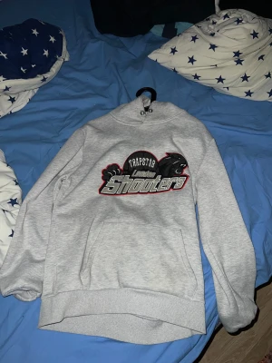 Grå Trapstar hoodie London Shooters - Säljer en grå hoodie från Trapstar med fett broderat London Shooters-tryck på bröstet och svart pantermotiv. Klassisk känguruficka framtill, huva och ribbade muddar. Perfekt för dig som gillar streetwear och vill sticka ut.