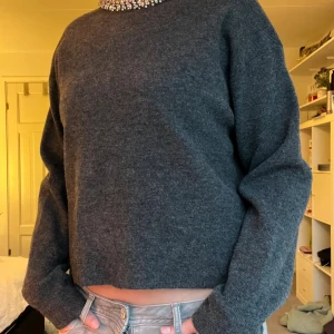 Mörkgrå stickad tröja med glittriga prälor/stenar  - Supersnygg mörkgrå stickad tröja med lång ärm och croppad passform. Runt halsen sitter glittriga pärlor/stenar. Den är super skön och har ett mjukt kvalite, men säljer då den inte kommer till användning☺️😊
