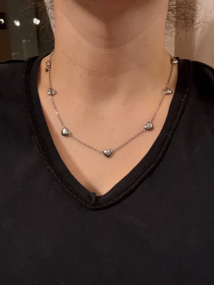 Halsband med hjärtan från Edblad - Snyggt halsband i silverfärgad metall från Edblad med flera små hjärtformade berlocker längs kedjan. Kedjan är tunn och har ett diskret Edblad-märke vid låset. Perfekt för dig som gillar stilrena och söta detaljer.