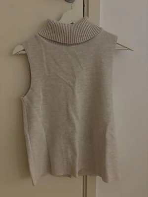 Beige stickad väst från Zara - Säljer en beige stickad väst från Zara med hög, ribbad polokrage. Västen är ärmlös och har en clean, minimalistisk look som är enkel att styla. Perfekt för lager på lager och riktigt mysig till höst och vinter. Köpt på vinted och va i fint skick och fint skick nu.