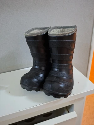 Svarta fodrade vinterstövlar - Säljer ett par svarta vinterstövlar med grov sula och högt skaft. Insidan är fodrad med mjukt material för extra värme. Utsidan har ett mönster med cirklar och ränder som ger en cool look. Perfekta för kalla dagar och snö.