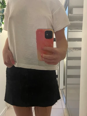 Svart jeanskjol med rå kant - Säljer en svart kort jeanskjol med rå, fransig kant nertill. Kjolen har klassisk femficksdesign och knapp framtill. Perfekt för dig som gillar en enkel men edgy stil. Passar till allt och är superenkel att styla. Från hm i strl 36.