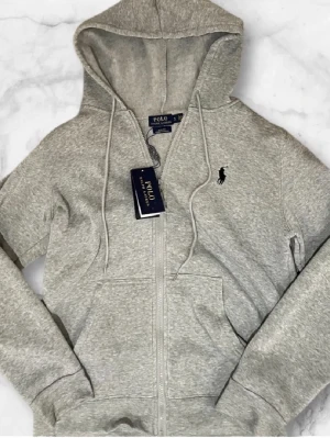 Ralph Lauren Zip Hoodie - En grå Ralph Lauren zip hoodie. Den är i ny skick, med lapp. Inga deffekter. Priset är inte slaget i sten!