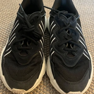 Adidas Ozweego sneakers  - Säljer ett par svarta adidas sneakers med vita ränder och chunky sula. Ovandelen är i mesh och mocka, med klassisk snörning och rund tå. Skorna har en sportig vibe och passar perfekt till streetwear eller casual outfits.