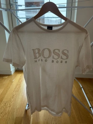 Vit t-shirt från Hugo Boss - Säljer en clean vit t-shirt från Hugo Boss med stort logotryck på bröstet. Klassisk rund hals och korta ärmar. Tillverkad i mjuk bomull som känns skön mot huden. Perfekt för dig som gillar stilrena och tidlösa plagg.