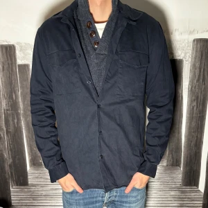 Mörkblå overshirt från Zara - Snygg mörkblå overshirt från Zara med klassisk krage och två bröstfickor med lock. Skjortan har knäppning framtill och är långärmad. Perfekt att bära öppen över en t-shirt eller stängd för en clean look.