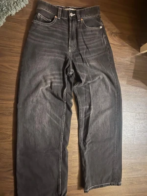 Svarta wide jeans från Bershka - Säljer ett par svarta jeans från Bershka i storlek 34. Byxorna har hög midja, raka ben och bred passform. Klassisk femficksmodell med kontrastsömmar och dragkedja fram. Perfekta för en avslappnad och trendig look.