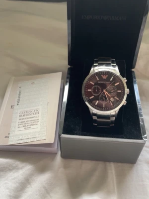 Armani klocka - . Bilderna visar en Emporio Armani-klocka i rostfritt stål med svart urtav runaway och certifikat.