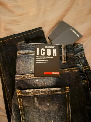 Dsquared2 ICON Ibrahimovic jeans - Säljer ett par Dsquared2 ICON Ibrahimovic jeans i mörkblå tvätt med slitningar och färgstänk för en riktigt edgy look. Klassisk femficksmodell med raka ben och kontrastsömmar. Tjock denim i bomull och snyggt Dsquared2-märke bak.