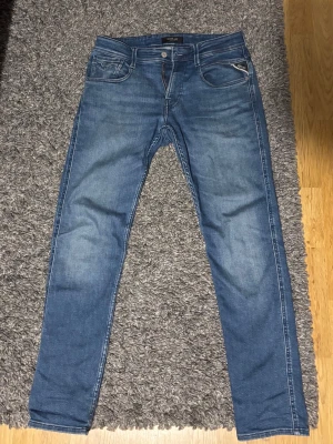 Blå Replay Anbass jeans herr Slim fit  - Säljer ett par blå Replay Anbass jeans med klassisk femficksdesign och snygga slitningar. Jeansen har normal passform, raka ben och är tillverkade i mjukt jeansmaterial. Märkeslogga på bakfickan och bakre linningen. Perfekta till vardagslooken. Storlek 29/30