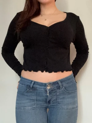 Svart topp med knappar - svart topp med lång ärm och v-ringning från BikBok. Toppen har dekorativa vågiga kanter nertill och knappar hela vägen framtill. strl M!!!