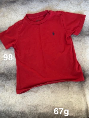 Röd t-shirt från Polo Ralph Lauren - Klassisk röd t-shirt från Polo Ralph Lauren med den ikoniska broderade loggan på bröstet. T-shirten har rund hals och korta ärmar, 🌸 Mindre fläck. Köpt i usa. Storlek 98