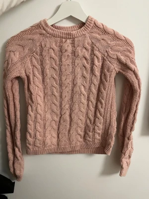 Rosa kabelstickad tröja från Bershka - Säljer en mysig kabelstickad tröja från Bershka i ljusrosa färg. Tröjan har rund hals, långärmade ärmar och ett chunky flätmönster över hela plagget. Perfekt för att hålla sig varm och snygg under kyliga dagar.