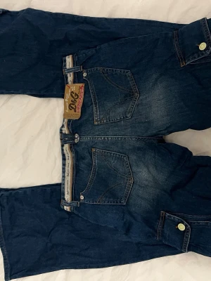 Blå jeans från Dolce & Gabbana - Säljer ett par snygga blå jeans från D&G med coola detaljer. Jeansen har är bootcut och köpta på humana. 