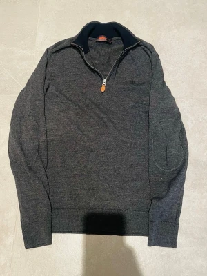 Morris q zip - Snygg mörkgrå tröja från Morris i 100% merinoull. Modellen har half zip med läderdetalj, ribbade muddar och förstärkta armbågar. Perfekt för dig som vill ha en stilren och bekväm tröja med klassisk look. Storlek m passar som s