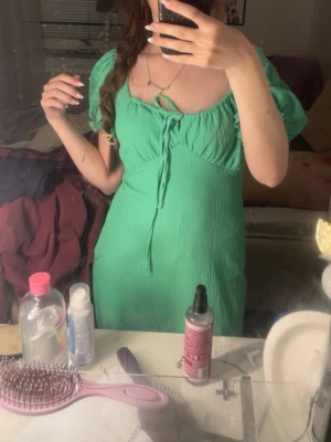 Grön kortklänning från Ellos - Snygg grön klänning från Ellos i storlek 34/36. Modellen har puffiga kortärmar med rynkade kanter och en söt snörning vid bysten. Materialet är strukturerat och känns mjukt mot huden. Klänningen har en feminin passform och är perfekt för vår och sommar.