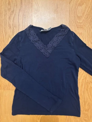 Mörkblå långärmad tröja från Gina Tricot - Marinblå långärmad tröja från Gina Young i storlek 146/152 med snygg spetsdetalj längs v-ringningen. Tillverkad i mjukt material som känns skönt. Säljer för att den är för liten. 