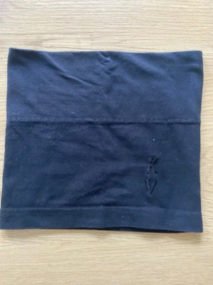 Kriminalvården Svart  tubhalsduk - Svart tubhalsduk i mjukt och stretchigt material med broderade initialer 'KV'. Kan användas som halsvärmare, pannband, mössa eller ansiktsmask. Perfekt för utomhusaktiviteter och enkel att styla på flera sätt.