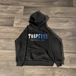 Trapstar Hoodie - Säljer en svart Trapstar hoodie i klassisk design med tryck framtill. En populär streetwear-hoodie som passar perfekt till vardagliga outfits.