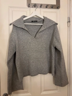 Grå stickad tröja med krage Gina Tricot - Mysig grå stickad tröja från Gina Tricot i storlek S. Tröjan har bred krage, v-ringad hals och långa ärmar med ribbade muddar. Passformen är loose och materialet känns mjukt och värmande, perfekt för kyliga dagar. Varsamt använd! 