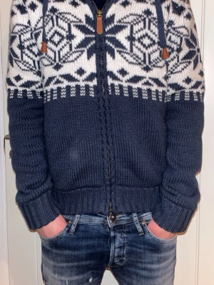 Mörkblå stickad hoodie med mönster - Säljer en mörkblå och vit stickad hoodie med dragkedja. Perfekt för kalla dagar när du vill vara både varm och stilren.