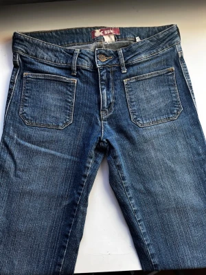Blå bootcut jeans från H&M, strl 170 - Säljer ett par klassiska blå jeans från H&M med bootcut passform. Jeansen har normal midja, vida ben (bootcut) och snygga kontrastsömmar. Tillverkade i slitstarkt denimtyg med två framfickor och bälteshällor. Perfekta till vardagslooken!