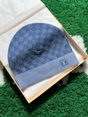 Blå rutig Louis Vuitton mössa/halsduk - Säljer en snygg blå mössa från Louis Vuitton med klassiskt rutigt mönster och LV-logga framtill. Mössan är stickad och har en bred kant nertill som ger en clean look. Perfekt accessoar för dig som vill ha något exklusivt och stilrent. Hela settet 2000kr (((OBS!!! Intressekoll!!!)))